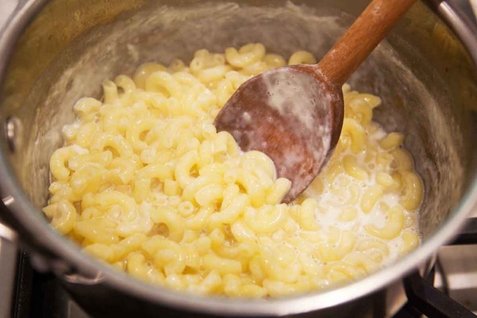 Macaroni and cheese being stirred by a wooden spoon in a copper pot