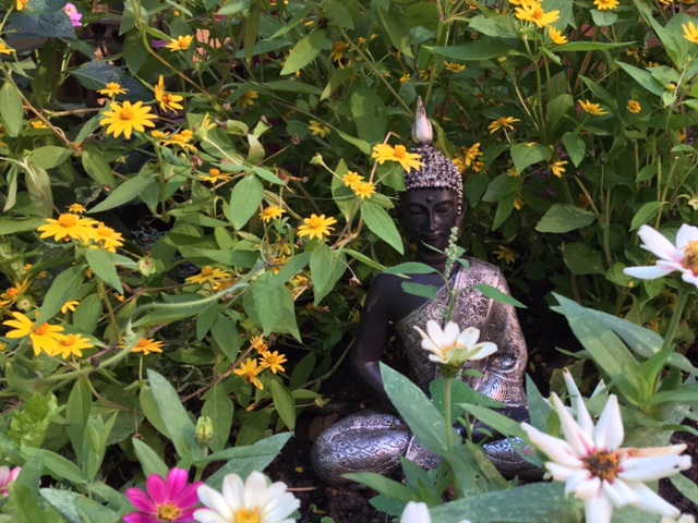 Statue of The Buddha surrounded by flowers in late summer