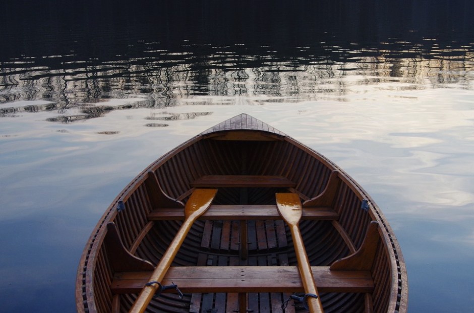 A wooden row boat sitting with quiet oars