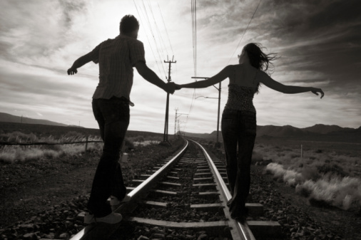 Young couple walking hand in hand on train track, rear view
